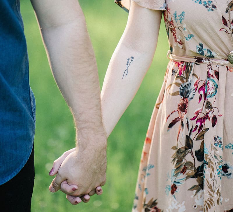A man and woman holding hands in the grass.