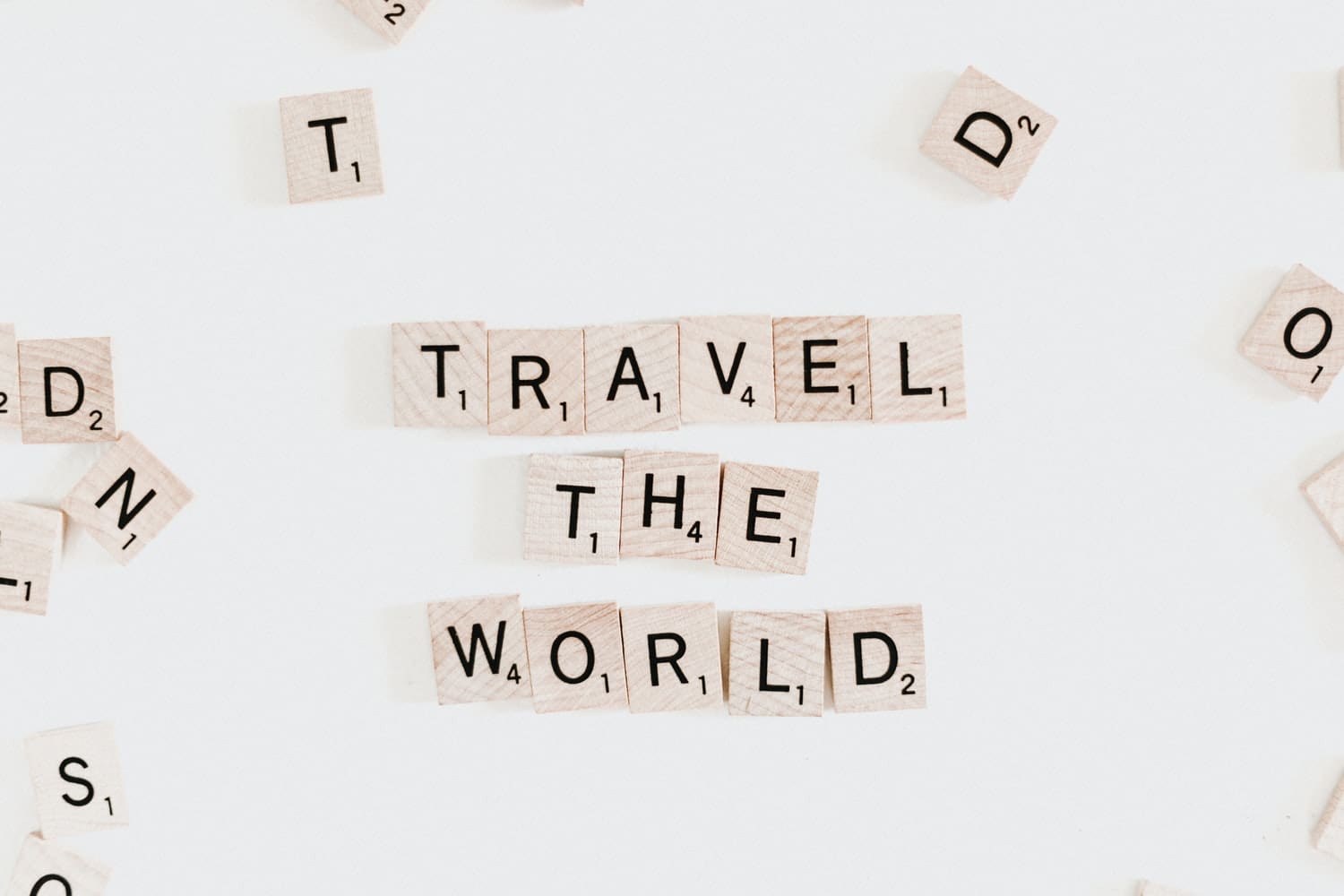 A word spelled out in scrabble tiles that say " travel the world ".